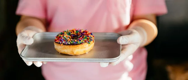 An image of a smiling customer at a donut shop counter, receiving a freshly made donut.